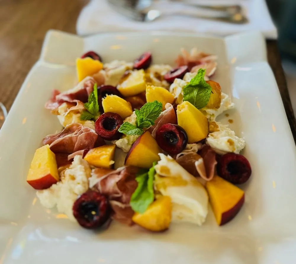 Salad with peaches, cherries, prosciutto, mozzarella, and fresh mint leaves on a white plate.