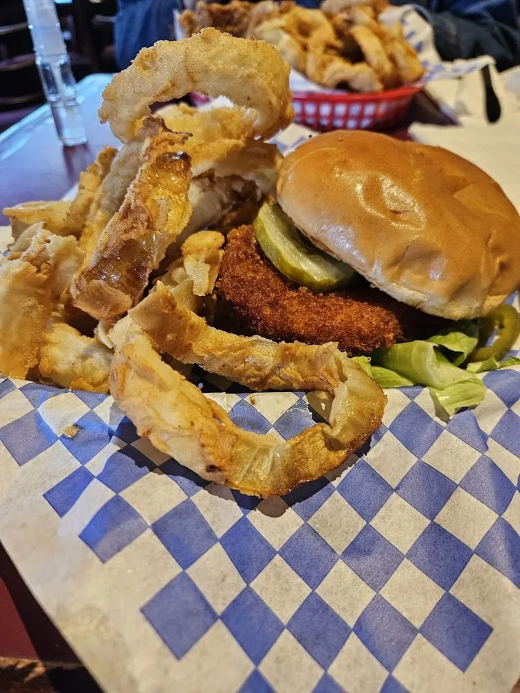 Fried chicken sandwich with pickles and lettuce, served with onion rings on blue checkered paper