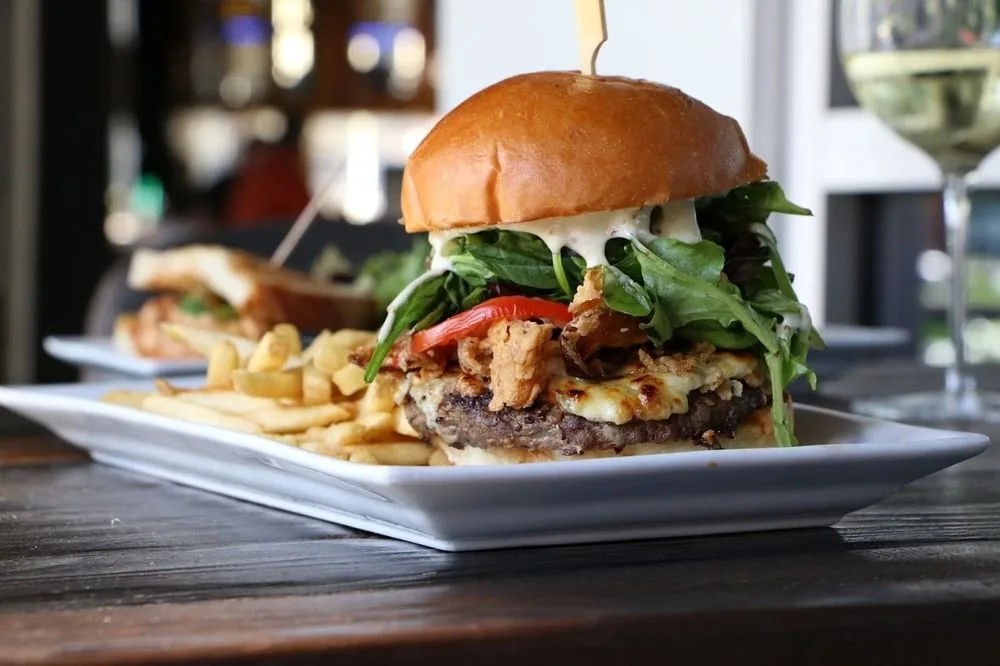 A hamburger with lettuce, tomato, fried chicken, melted cheese, and a toasted bun, served with French fries on a white plate.